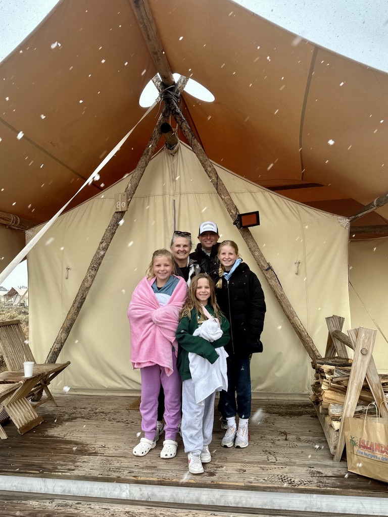 Family glamping in a canvas tent during a Colorado snow flurry, dad in a custom patch hat