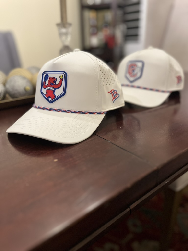 Two Cherry Creek Bruins tennis hats on a table, one with the bear patch in focus