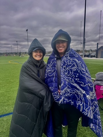 Two parents bundled in blankets on the sideline of a chilly Colorado lacrosse field