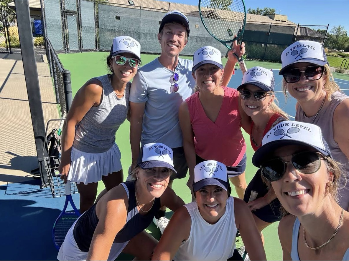 Tennis group on the court wearing custom navy and white At Your Level trucker hats